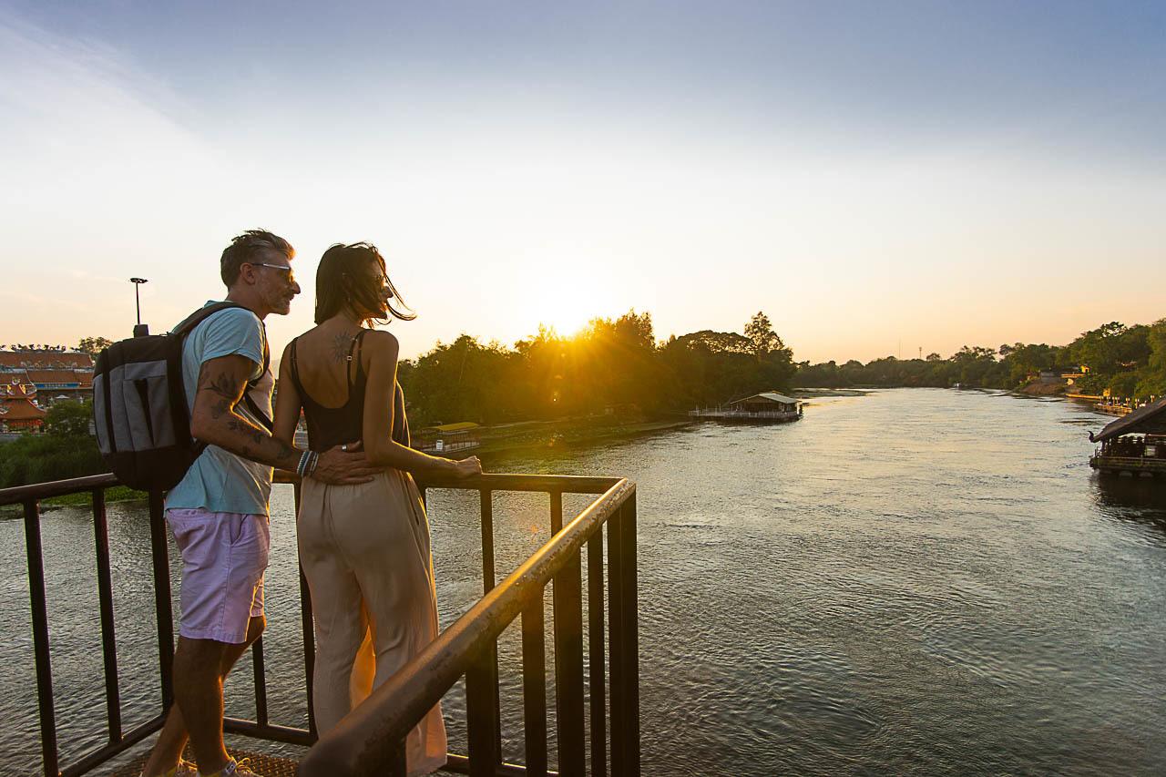 Couple walking over the River Kwai Bridge during sunset.